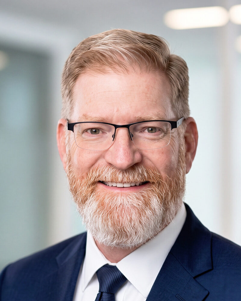 Portrait of Eddie Burroughs, a bearded man in a navy suit and tie.